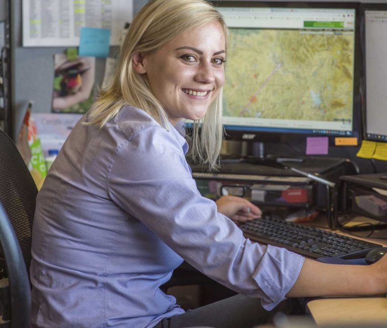 A woman in business attire sitting at a desk working at a computer.